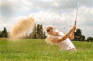 Female golfer tossing up dirt and dust after hitting her ball out of a sand trap.